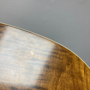 Close-up view of the curved wooden edge and polished surface of a Waterloo WL-12 Parlor Acoustic guitar by Waterloo, with visible wood grain and finish, set against a gray wall.
