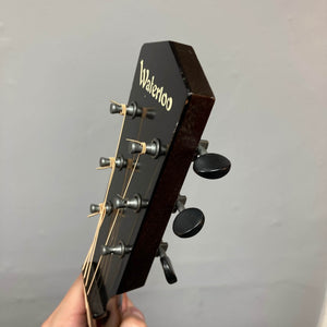 A close-up of the headstock of a Waterloo WL-12 Parlor Acoustic w/Case Used Consign guitar shows tuning pegs, strings, and the "Waterloo" logo against a plain gray background.