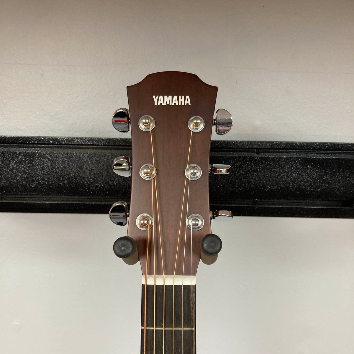 A close-up of the headstock of a Yamaha A3M ARE Vintage Natural Acoustic Guitar w/Hard Bag Used showcases the tuning pegs and Yamaha logo as it rests on a wall hanger. The image draws attention to premium features such as its solid mahogany construction and suggests innovative elements like the advanced SRT2 pickup system.
