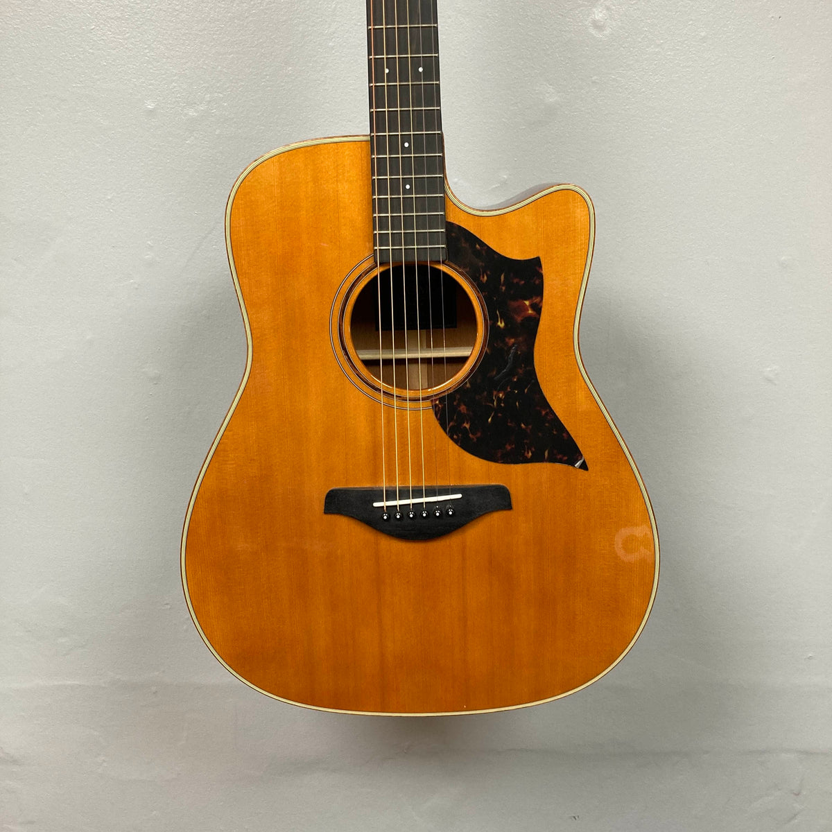 Yamaha A3M ARE Vintage Natural Acoustic Guitar with cutaway body, solid mahogany construction, wood finish, black pickguard, and six strings, pictured against a plain light gray wall.