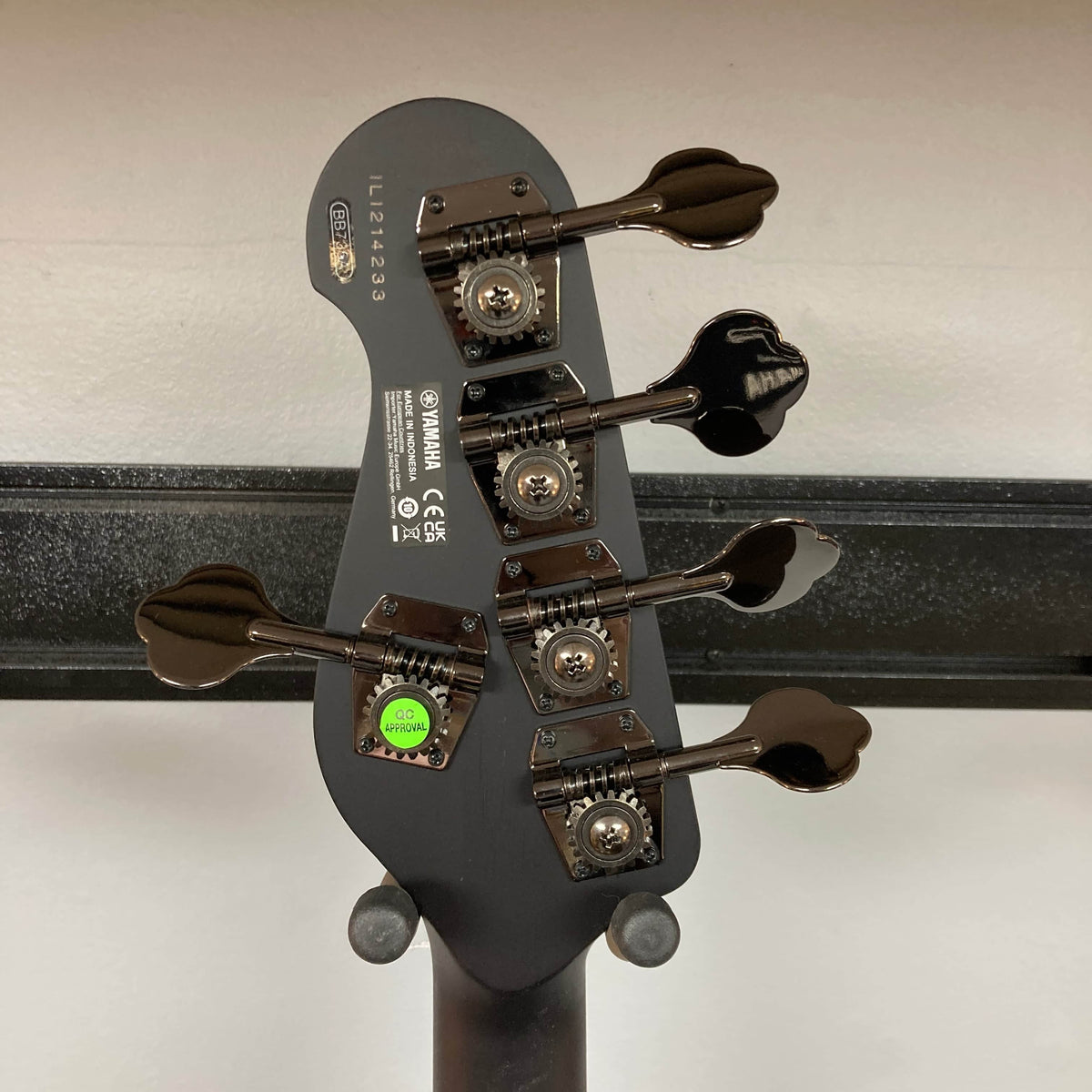 Close-up of the back of a Yamaha BB735A Electric 5-String Bass Coffee Sunburst (Blem Discount) headstock showing four tuning pegs, manufacturer labels, serial numbers, and a green "QC PASSED" sticker against a neutral background.