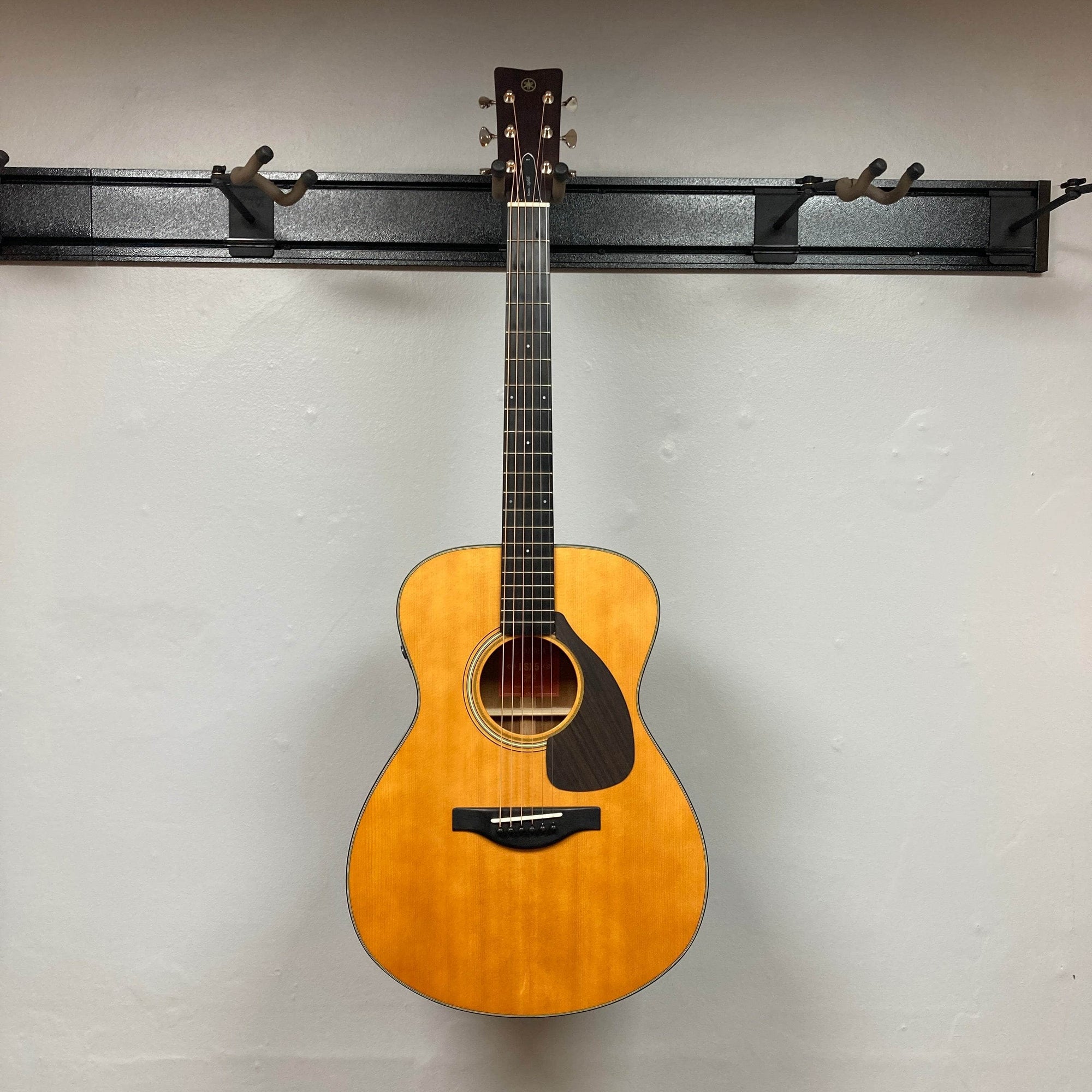 The Yamaha FSX5 Satin Red Label Natural Made In Japan w/Case, an acoustic electric guitar by Yamaha, is shown front-facing against a plain light gray wall, highlighting its body, sound hole, pickguard, and part of the neck.