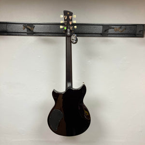 A Yamaha Revstar Standard RSS02T electric guitar in Vintage White, with a chambered mahogany body, hangs on a wall rack. Shown from the back, it has a tag on one tuner and comes with a gigbag.