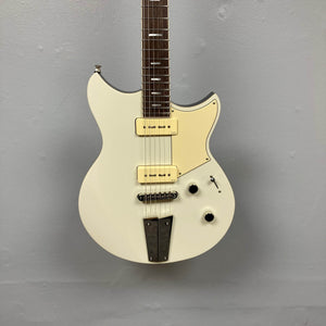 A Yamaha Revstar Standard RSS02T Vintage White electric guitar with P90 pickups and a chambered mahogany body hangs against a plain gray wall. Comes with a gigbag.