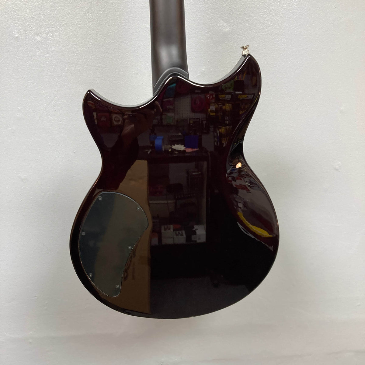 The image shows the back of a Yamaha Revstar Standard RSS02T Vintage White electric guitar with a glossy finish, reflecting shelves and items from the room. The guitar is positioned against a plain white wall.