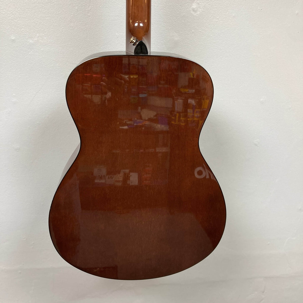 The Yamaha Storia III Solid Mahogany Top Concert guitar features a glossy brown mahogany top that reflects shelves and items from the surrounding room.
