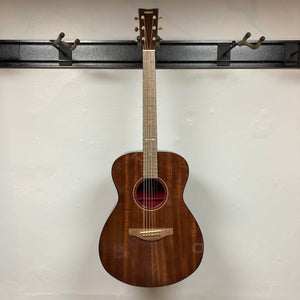 A Yamaha Storia III Solid Mahogany Top Concert guitar hangs on a black wall-mounted holder against a plain white wall.