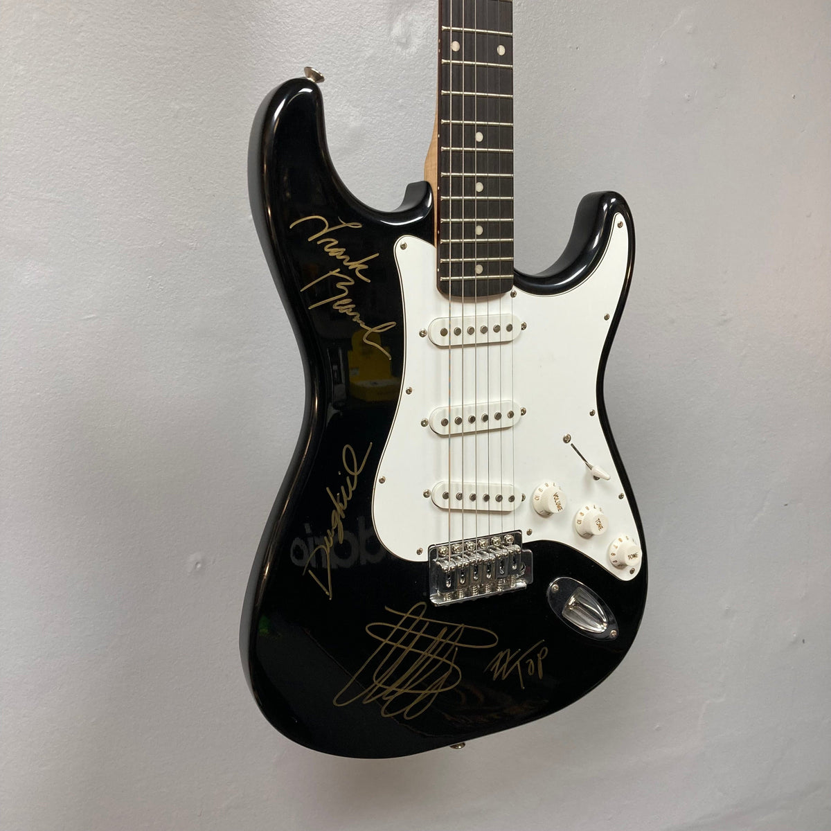 ZZ Top Signed Strat Style Guitar with autographs by Billy Gibbons, Dusty Hill, and Frank Beard displayed on a wall.