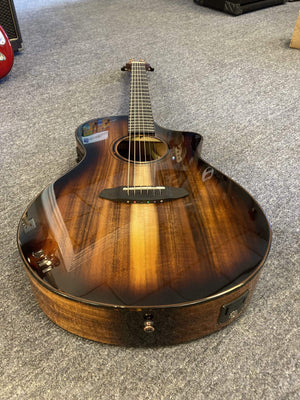 Breedlove Pursuit Exotic S Concert Edgeburst CE Koa-Koa guitar on a carpet, showcasing its elegant design and superior EcoTonewood technology.