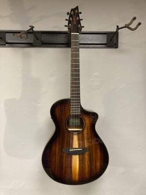 Breedlove Pursuit Exotic S Concert Edgeburst CE Koa-Koa guitar leaning against a white wall, showcasing its sleek design and premium finishes.