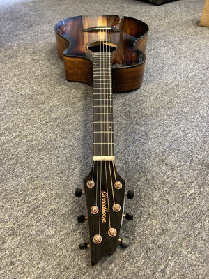 Breedlove Pursuit Exotic S Concert Edgeburst CE guitar, koa wood, lying on showroom floor, showcasing its gloss finish and intricate tortoise binding.