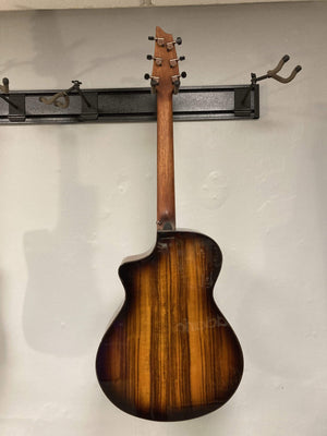 Breedlove Pursuit Exotic S Concert Edgeburst CE Koa-Koa guitar hanging on a wall, showcasing its glossy finish and tortoise binding.