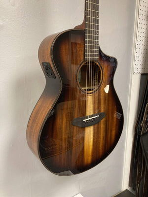 Breedlove Pursuit Exotic S Concert Edgeburst CE Koa-Koa guitar, featuring a gloss finish and tortoise binding, hanging on a wall.