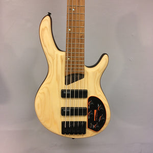 Cort Artisan B5 Element Natural electric bass guitar featuring a wooden body with black hardware, displayed on a wall.