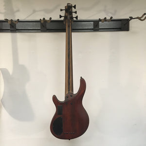 Cort Artisan B5 Element Natural bass guitar mounted on a wall, showcasing its wooden neck, fretboard, and body details.