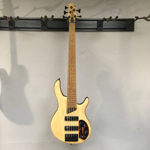 Cort Artisan B5 Element Natural bass guitar mounted on a wall, showcasing its sleek design and high-quality craftsmanship.