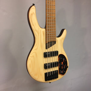 Cort Artisan B5 Element Natural electric bass guitar with a wooden body, mounted on a wall, showcasing its neck and strings.