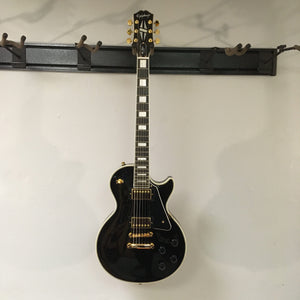 2022 Epiphone Les Paul Custom Ebony with gold hardware and block inlays, featuring Gibson pickups, displayed on a wall-mounted rack.