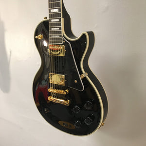2022 Epiphone Les Paul Custom Ebony, featuring gold hardware, Gibson pickups, and white binding, displayed against a wall. Comes with a Gator case.