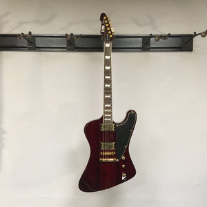 ESP LTD Phoenix-1000 electric guitar on a wall, featuring gold hardware and Fishman Fluence Modern Humbucker pickups in See Thru Black Cherry finish.