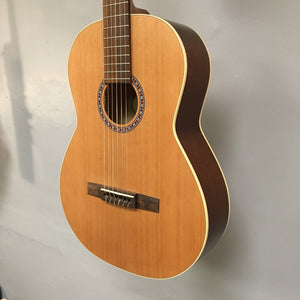 Godin Etude Classical Guitar Open Box, showcasing its solid cedar top, Canadian wild cherry back and sides, and rosewood fingerboard, mounted on a wall.