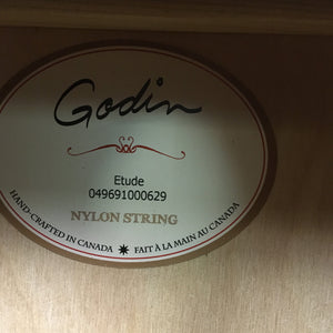 Godin Etude Classical Guitar Open Box, featuring a solid cedar top and rosewood fingerboard, displayed with a detailed label on a wooden surface.