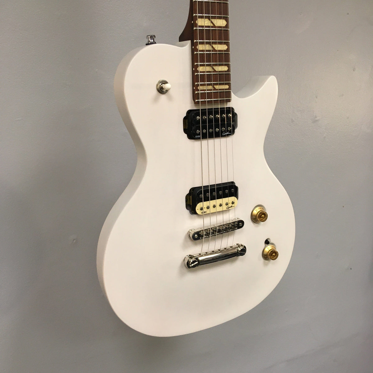 Godin Summit Classic HT Trans White Electric Guitar with black and gold hardware, mounted on a wall, featuring dual humbuckers, carved maple top, and semi-gloss finish.