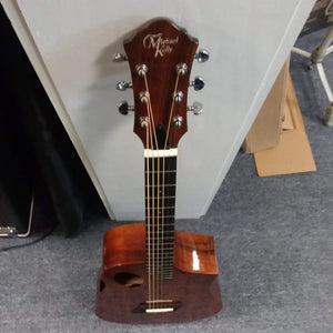 Michael Kelly Forte Koa Jr. travel guitar leaning against a wall, showcasing its koa body and compact design.