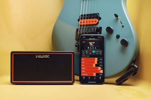 NUX Mighty Air wireless guitar/bass amplifier next to a guitar, showcasing its compact design and integrated Bluetooth connectivity for enhanced tone control via mobile app.