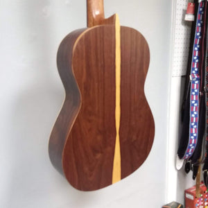 Ortega Nylon String Guitar R189SN-25TH with strap, hanging on a wall, includes 25th Anniversary gig bag.