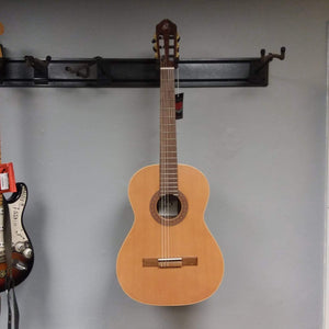 Ortega Nylon String Guitar R189SN-25TH with bag displayed on a wall, highlighting its solid cedar top and Granadillo back and sides.