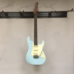 Schecter Nick Johnston Traditional Atomic Frost electric guitar on a wall hook, featuring a sleek design with brass inlays and Schecter locking tuners.