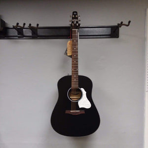 Seagull S6 Classic A/E Black guitar with white and black strap, semi-gloss finish, mounted on a wall.