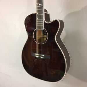 Seagull Artist Mosaic CH CW GT EQ Bourbon Burst guitar with solid spruce top and cutaway, leaning against a white wall.